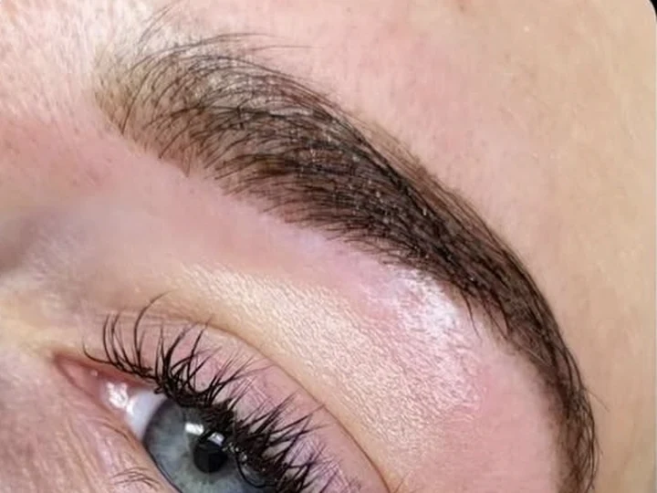 Volle bruine wenkbrauw na een brow treatment met verven, boven een blauwgrijs oog